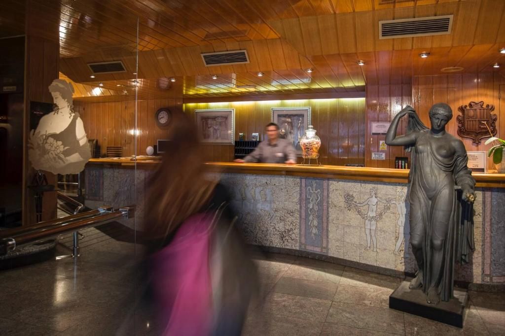 Un vestíbulo de hotel con una recepción, una estatua de mujer y un reloj en la pared.