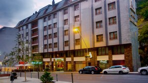 Un hôtel à plusieurs étages, doté d’une façade en pierre, de nombreux balcons et donnant sur la rue, où l’on peut voir des voitures garées et un trottoir pour les piétons.