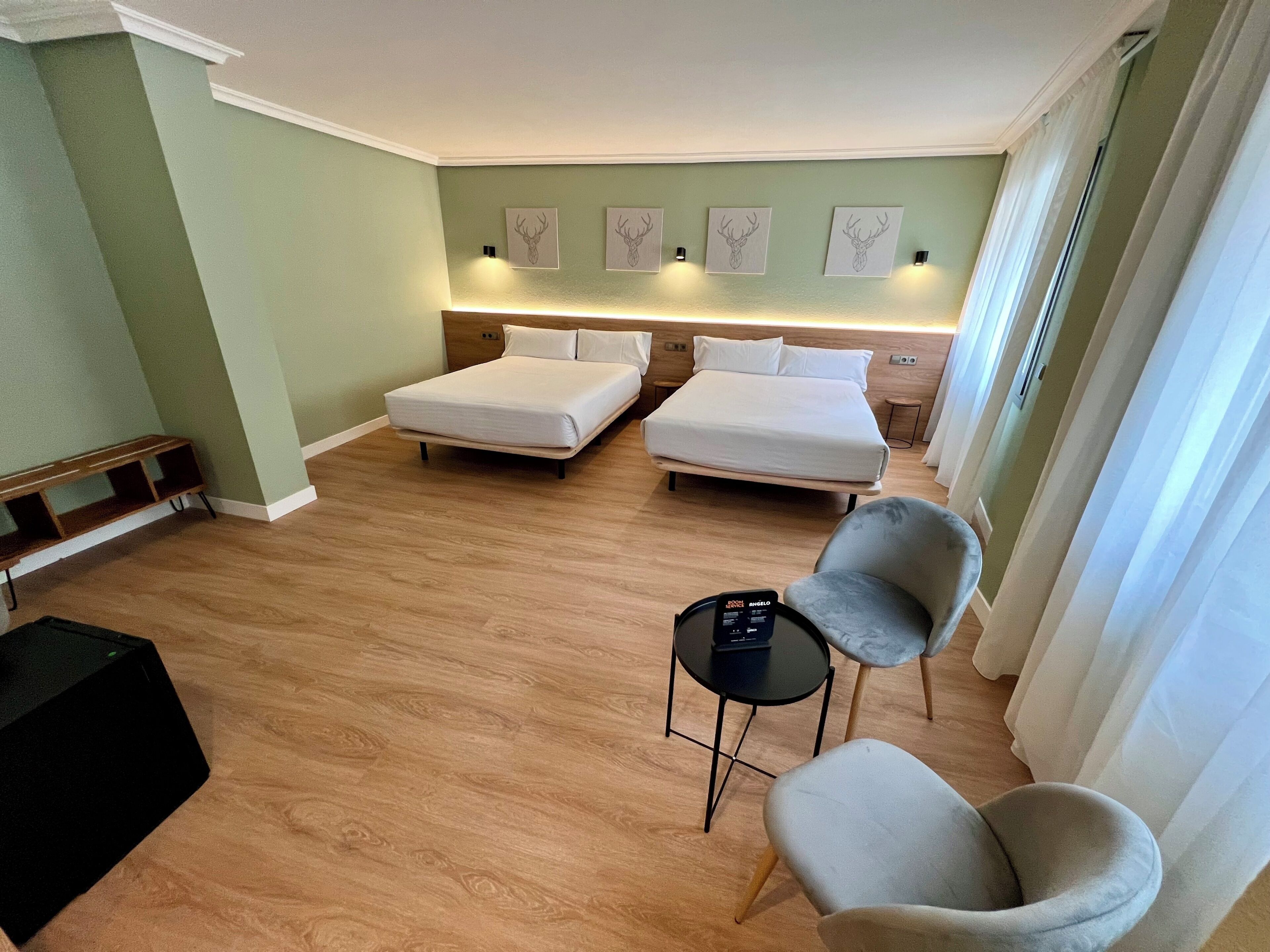 Habitació d'hotel amb dos llits, una taula petita, una cadira i una obra d'art a la paret.