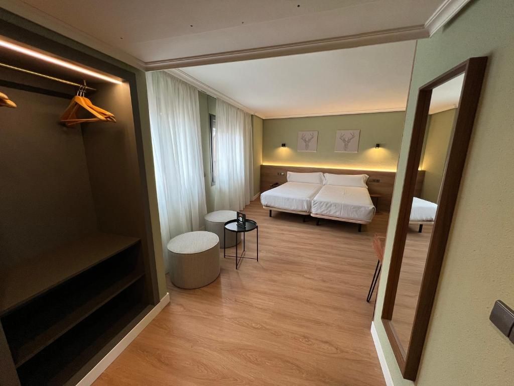 Habitación de hotel con cama, mesitas de noche, espejo, armario y zona de estar con una mesa redonda y sillas.