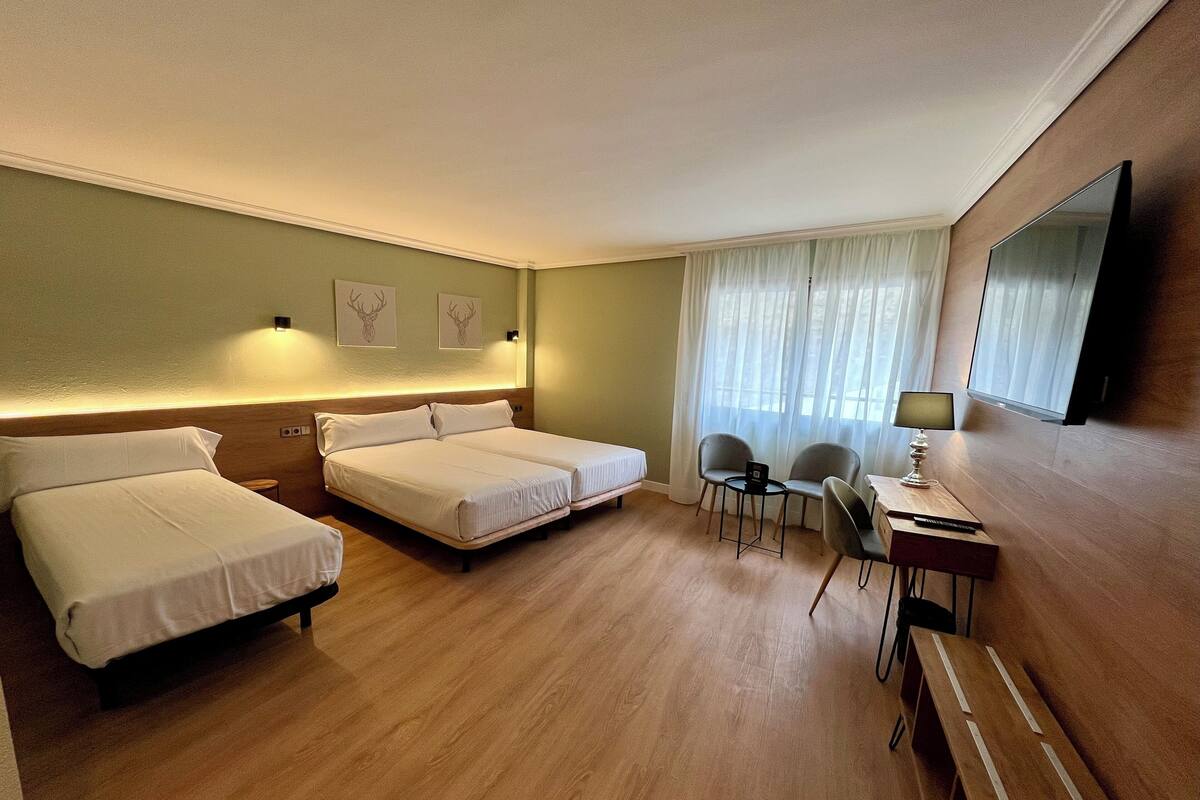 Een hotelkamer met twee bedden, een bureau met stoel, een televisie en een raam met gordijnen.