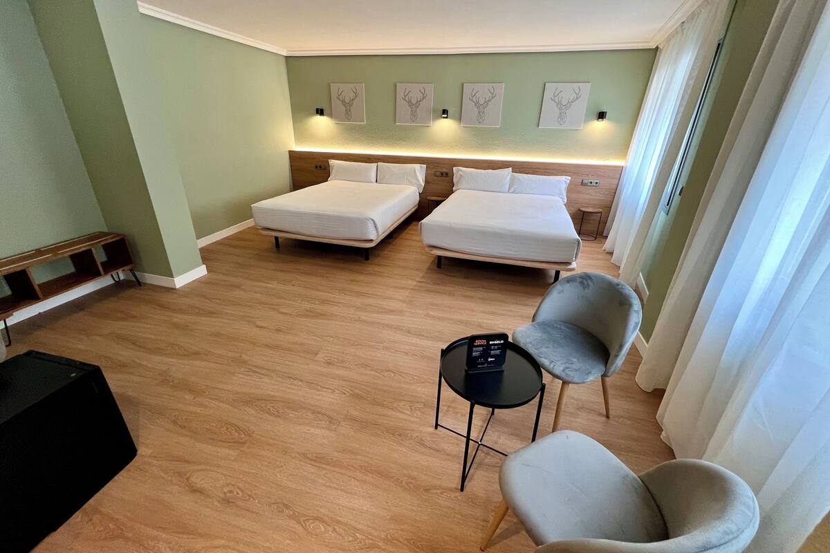 Een hotelkamer met twee bedden, een tafeltje, twee stoelen en een kunstwerk aan de muur.