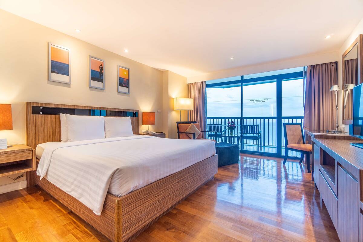 A hotel room with a large bed, a desk, and a balcony with a view.