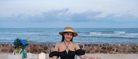 A table set with plates of food, a candle, and a vase with flowers by the ocean.
