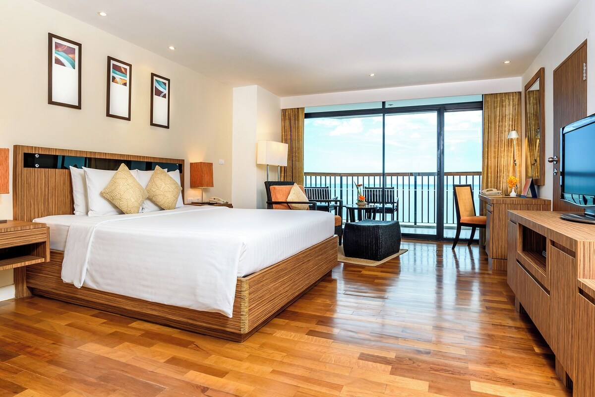 Une chambre d’hôtel avec un grand lit, un plancher en bois, un balcon avec des sièges et une télévision.