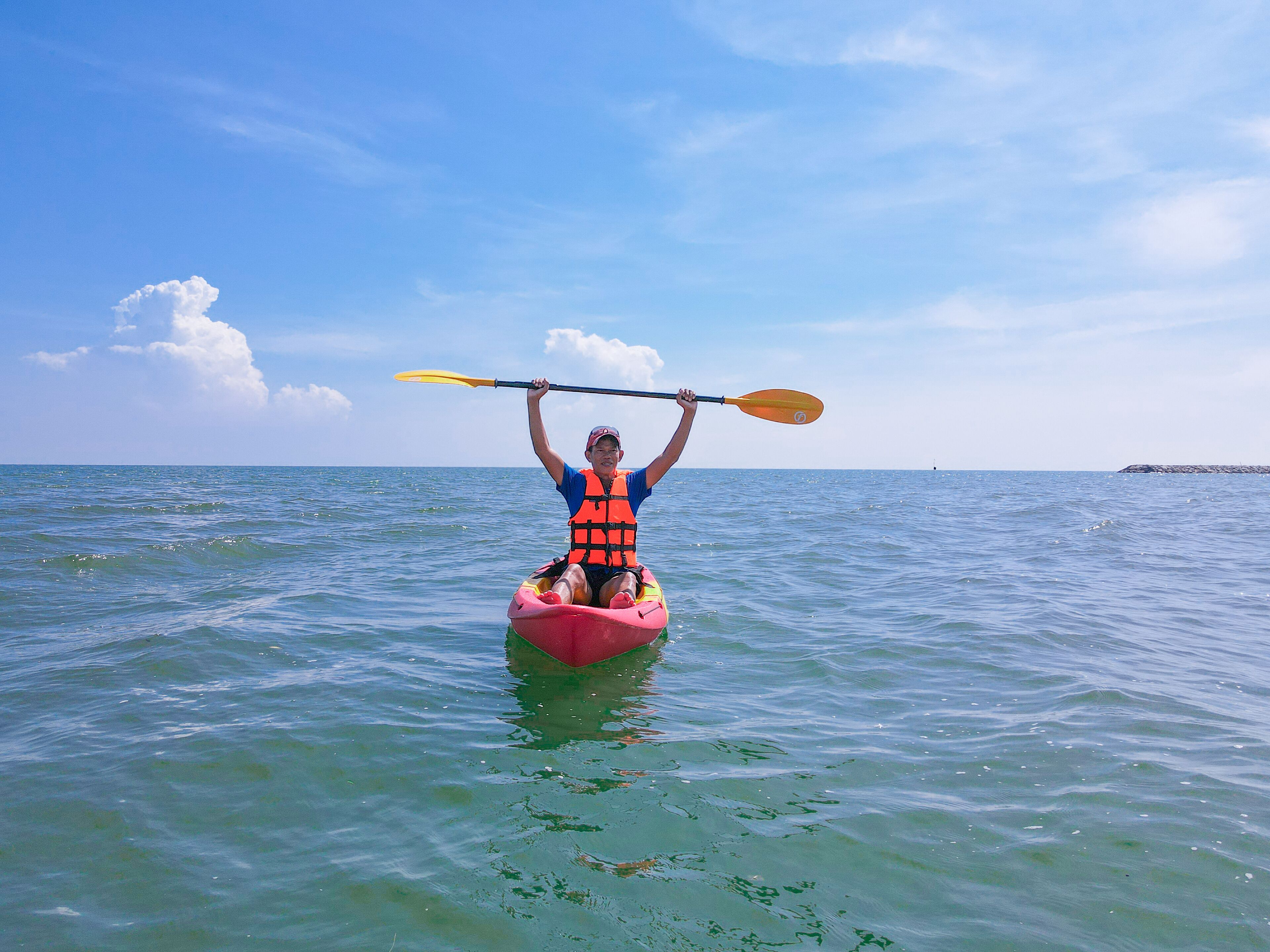Eine Person paddelt mit einem Kajak auf ruhiger See unter blauem Himmel.