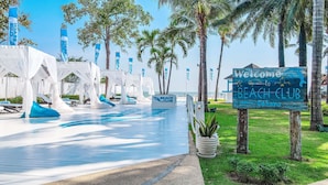 Un club de playa con piscina, sillas de descanso y palmeras.