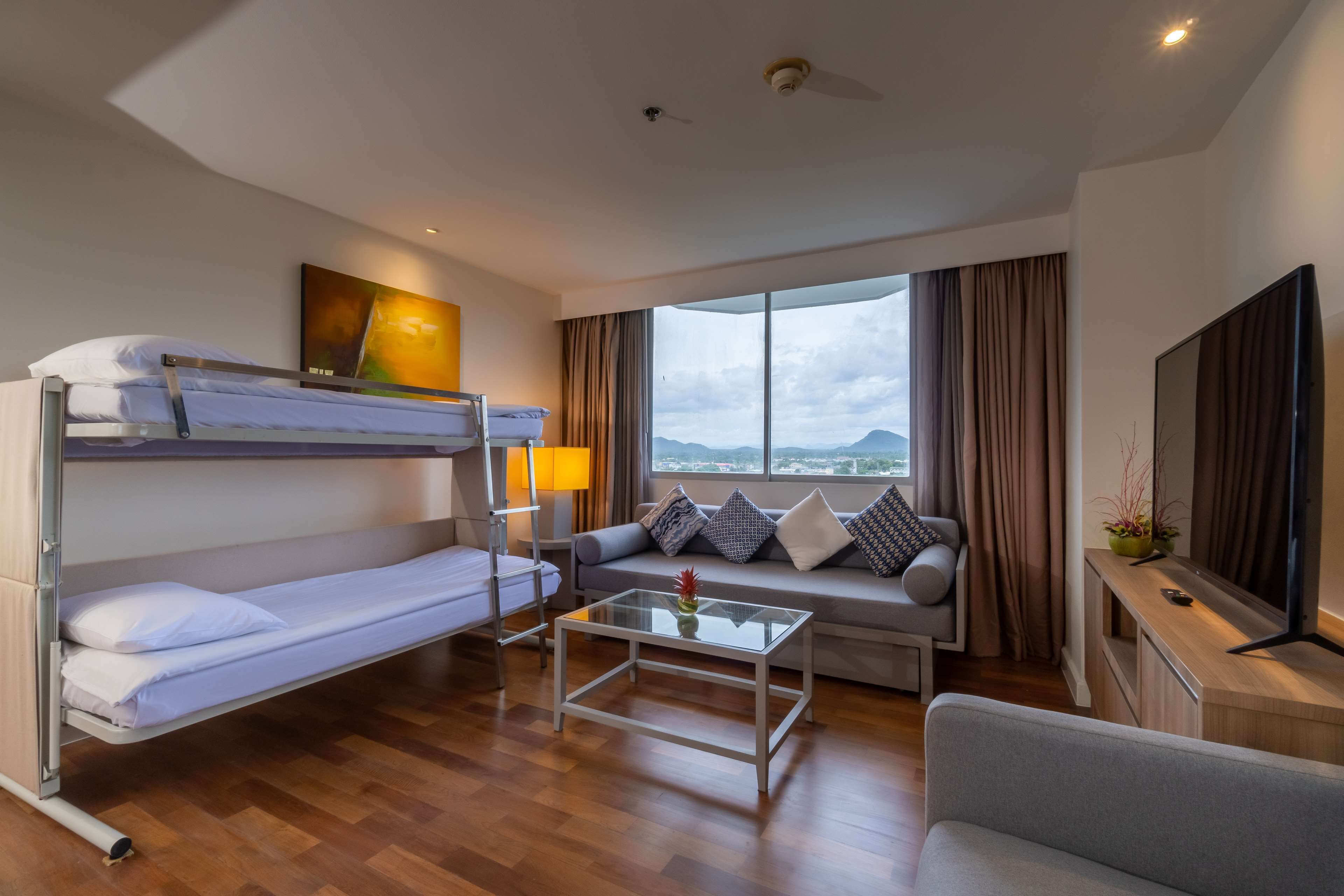 A modern hotel room with a bunk bed, a sofa, a coffee table, and a TV.