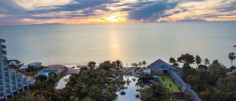 Un complexe hôtelier doté d’une piscine, de palmiers et offrant une vue sur le coucher de soleil sur l’océan.
