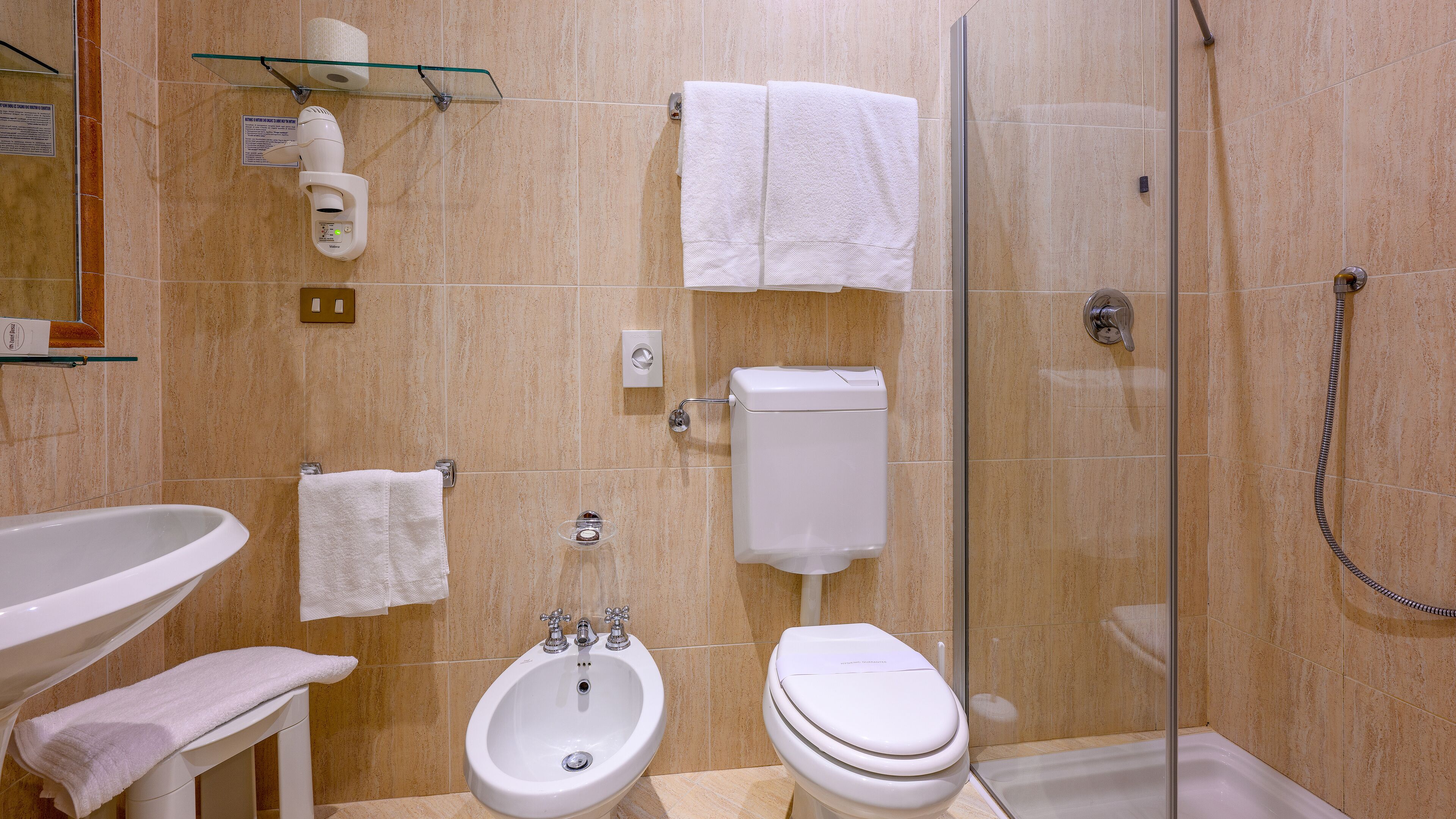 A bathroom with a sink, bidet, toilet, and glass shower enclosure.