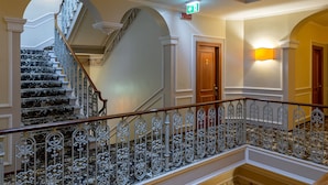 Un grand escalier orné de rampes en métal ouvragé et un palier au deuxième étage agrémenté d’une balustrade décorative.