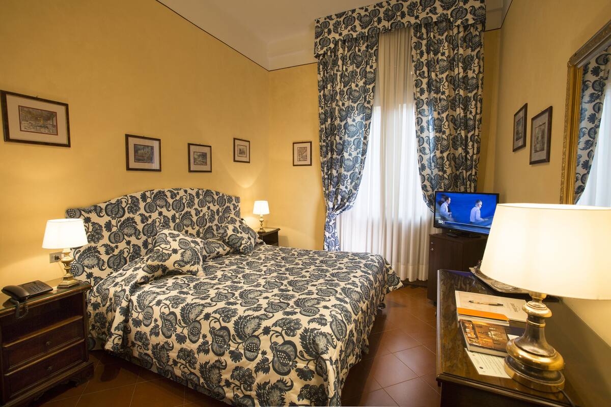 Una habitación de hotel con cama, lámparas de noche, televisión y cuadros en la pared.