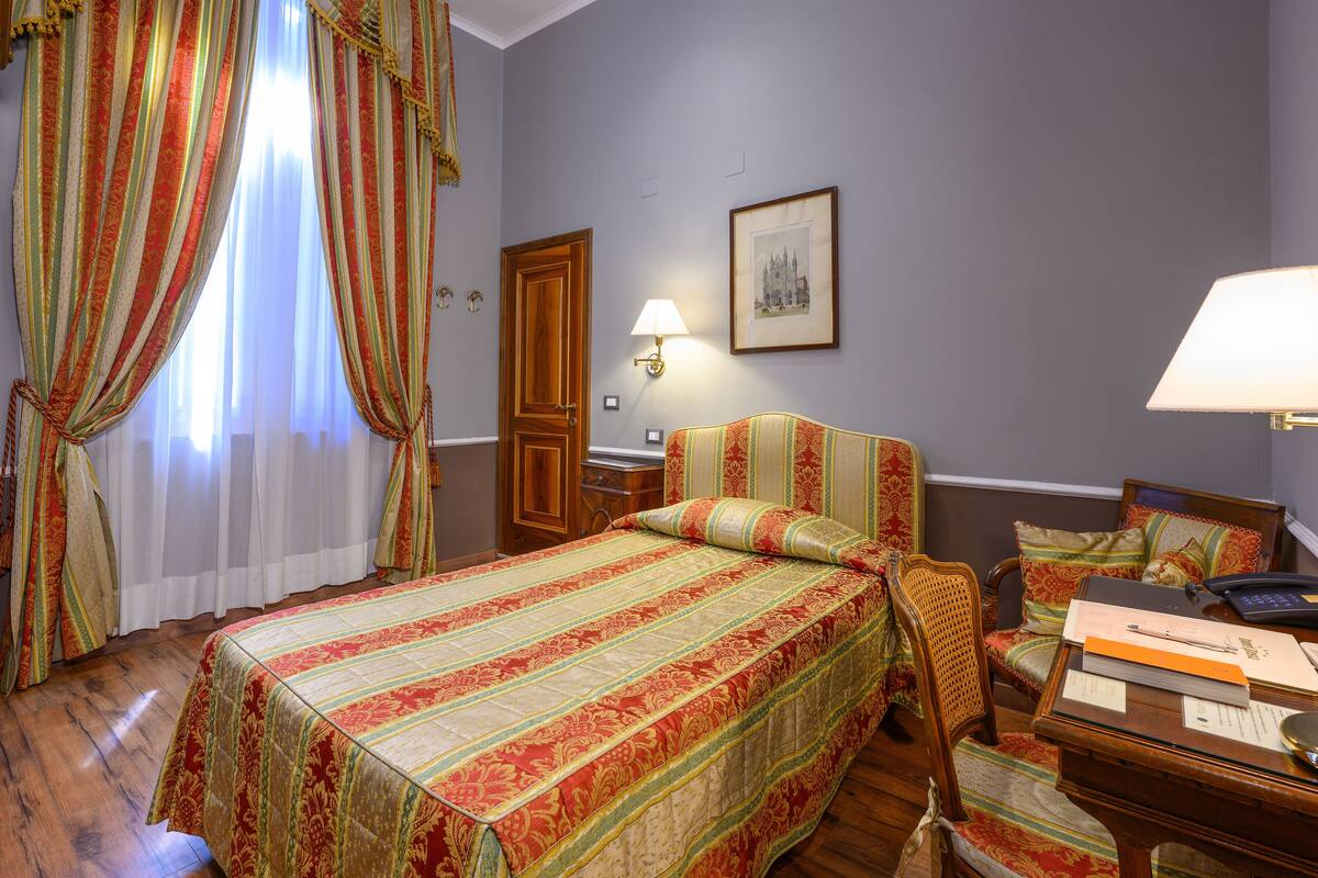 Habitación de hotel con una cama grande, una mesita de noche de madera, un escritorio con lámpara y una silla.
