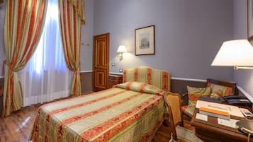 Habitación de hotel con una cama grande, una mesita de noche de madera, un escritorio con lámpara y una silla.