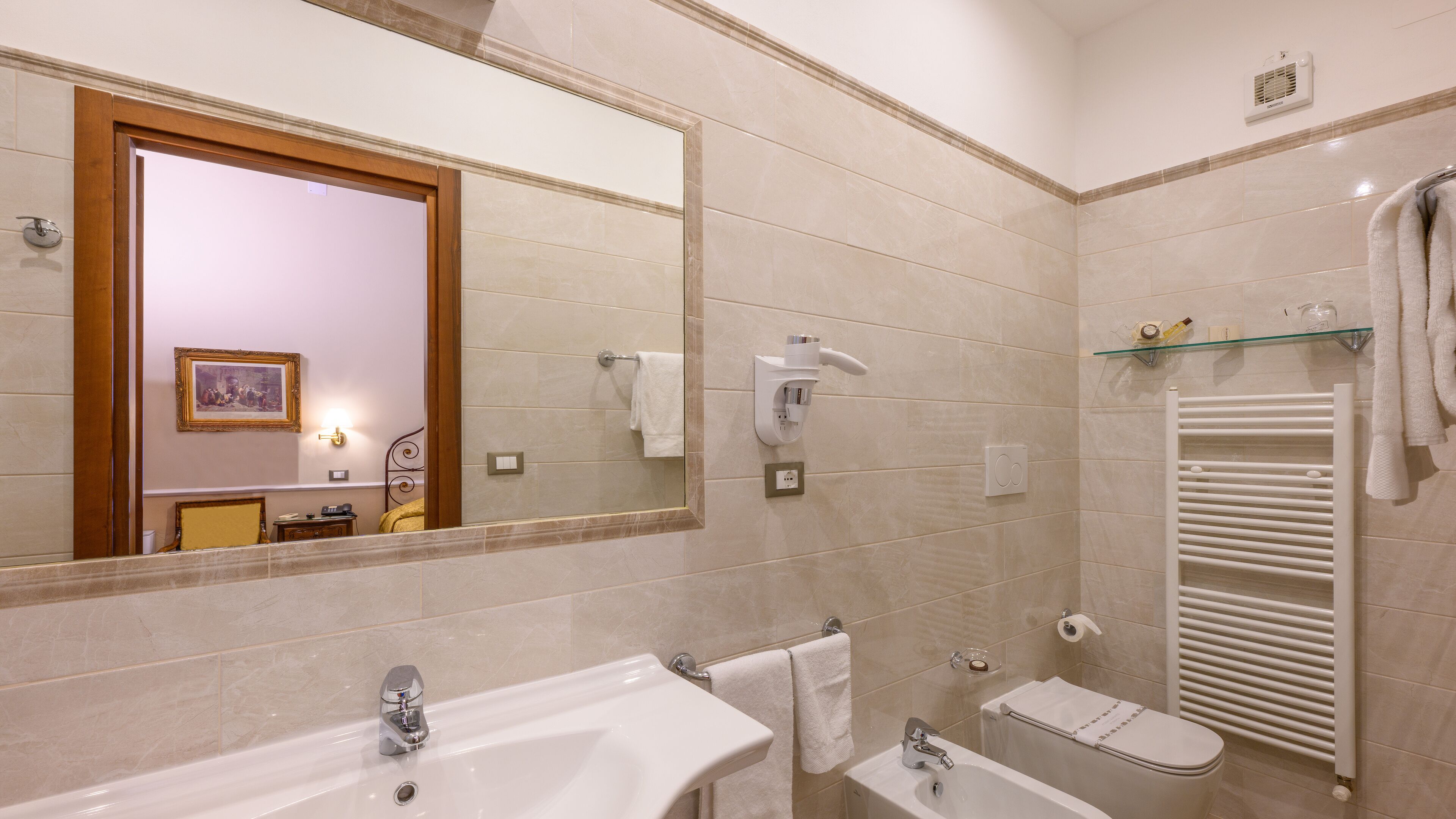 Ein modernes Badezimmer mit einem großen Spiegel, zwei Waschbecken, einer Toilette und einem Handtuchhalter.