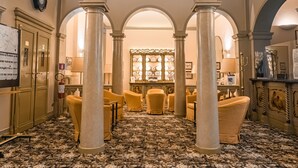 Un hall d’hôtel avec un tapis à motifs, des chaises jaunes et une présentation centrale d’assiettes.