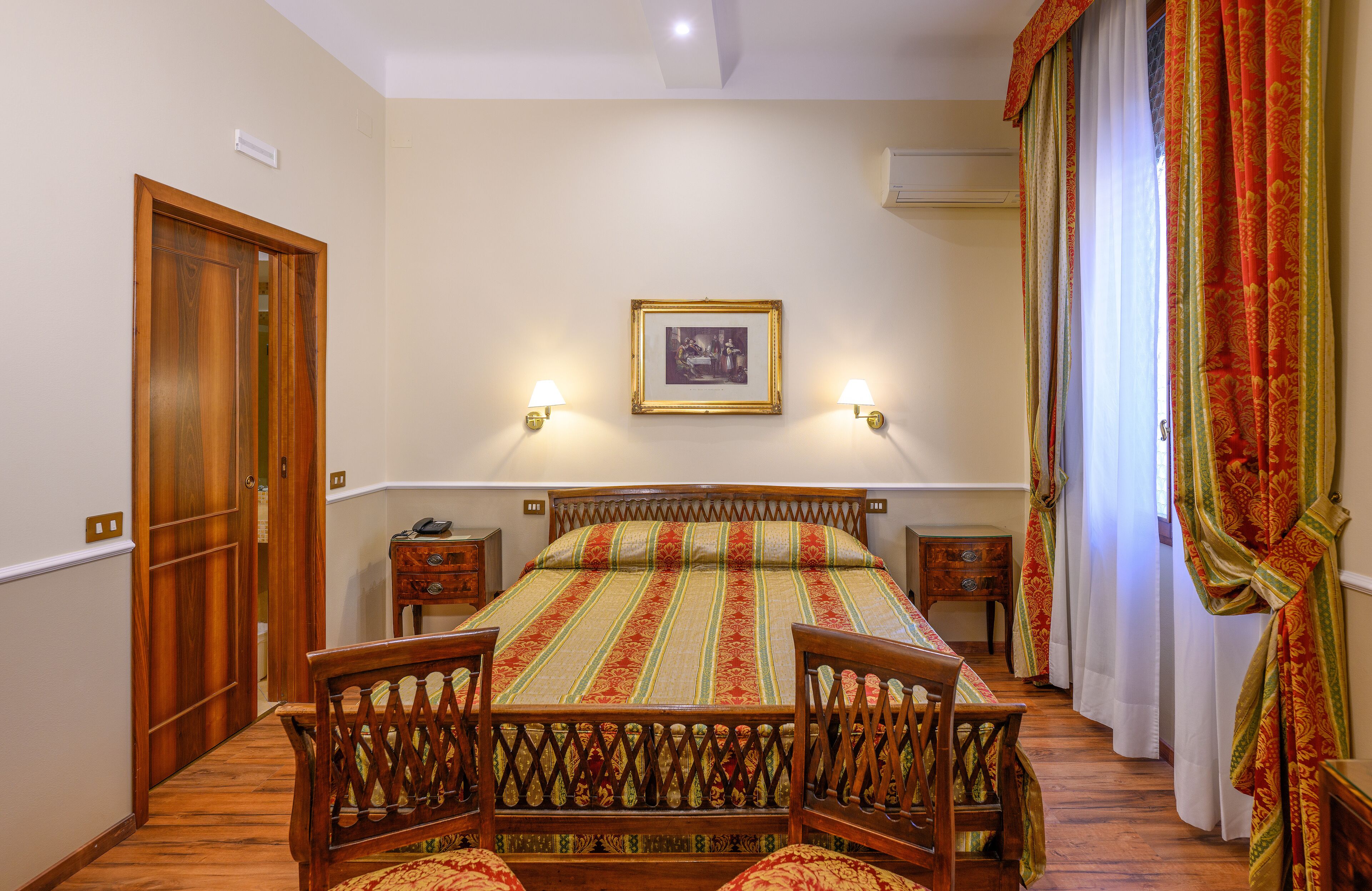 A bedroom with a wooden bed, two bedside tables, a nightstand, a chair, and a picture on the wall.