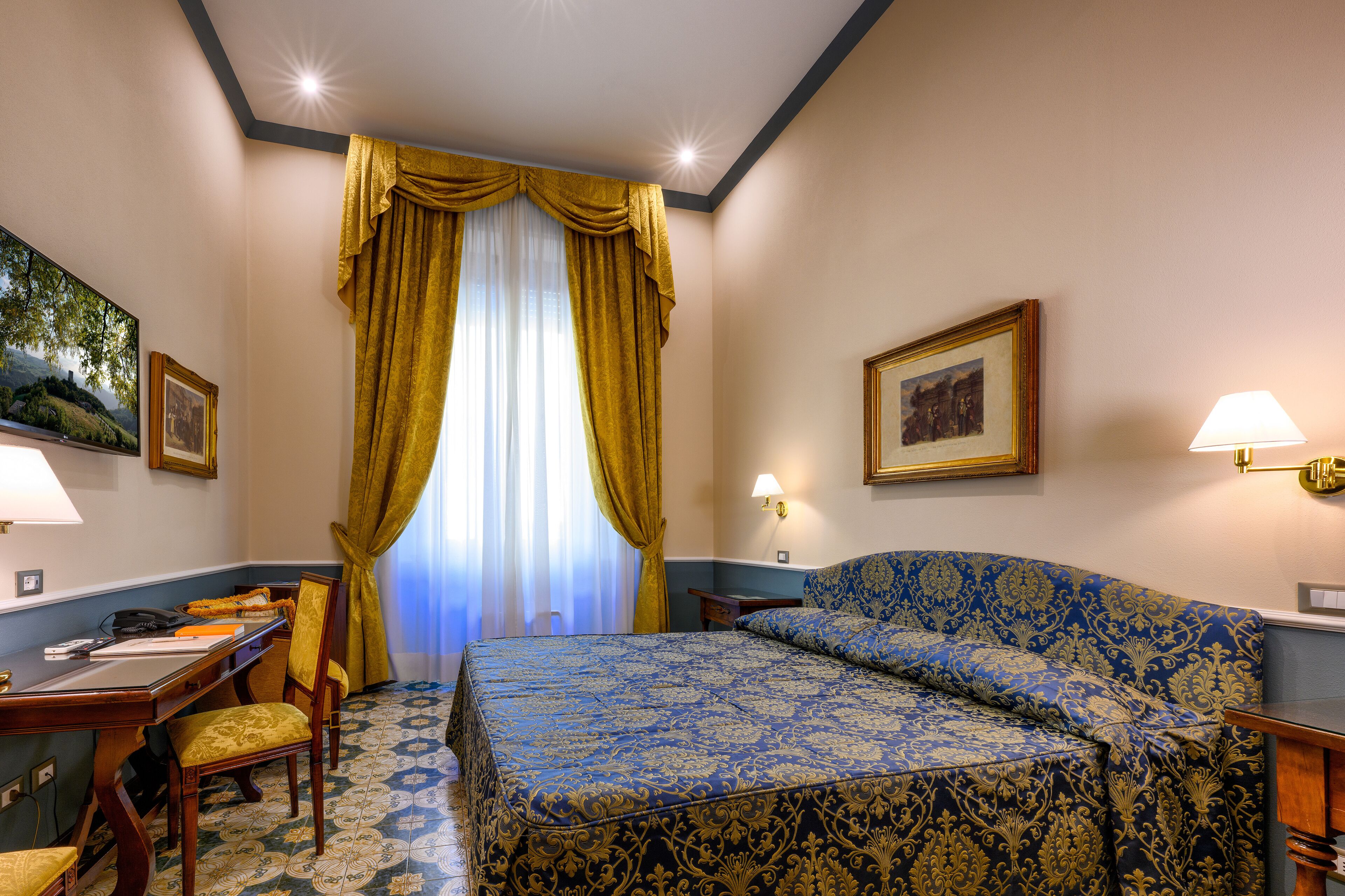 Une chambre d’hôtel avec un lit, un bureau, une chaise et une fenêtre avec des rideaux.