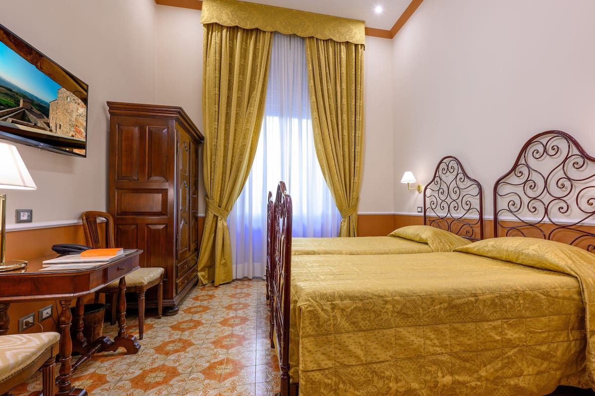 Una habitación de hotel con cama, escritorio, silla, armario y un cuadro en la pared.