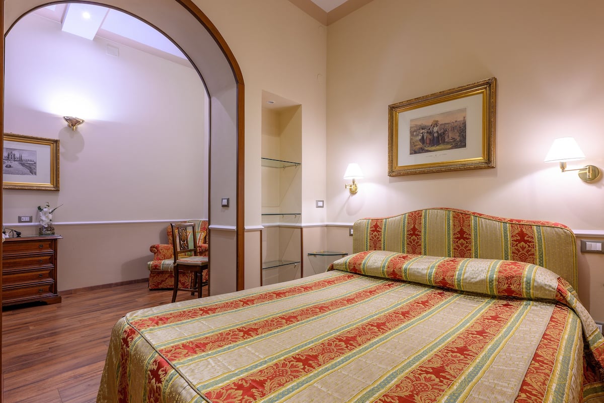 Una habitación de hotel con cama, una silla, cómoda y espejo.