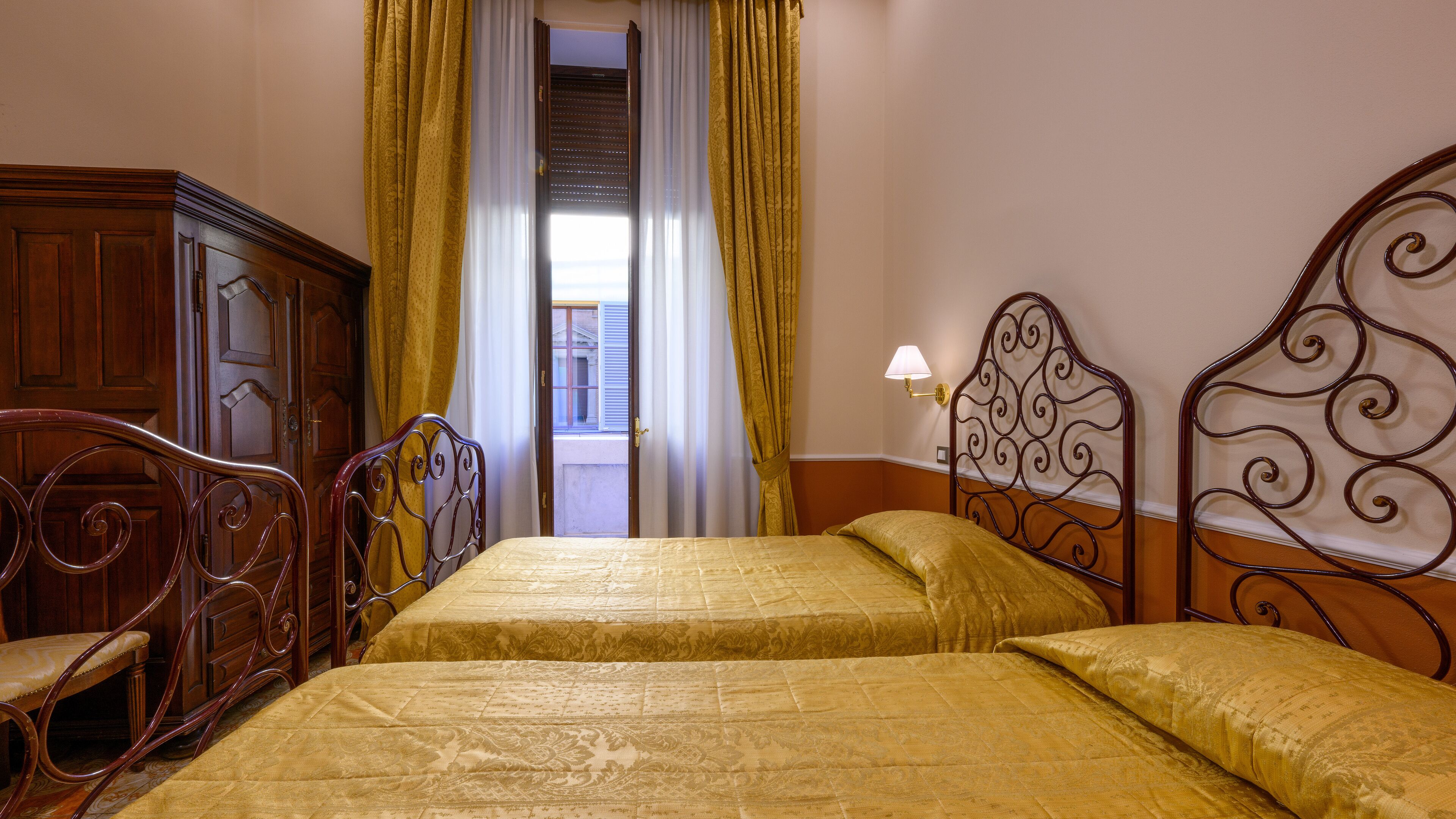 Habitación de hotel con dos camas, muebles de madera y vista a la calle a través de una ventana.