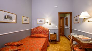 Habitación de hotel con una cama individual, un escritorio con silla, un armario de madera y cuadros enmarcados en las paredes.