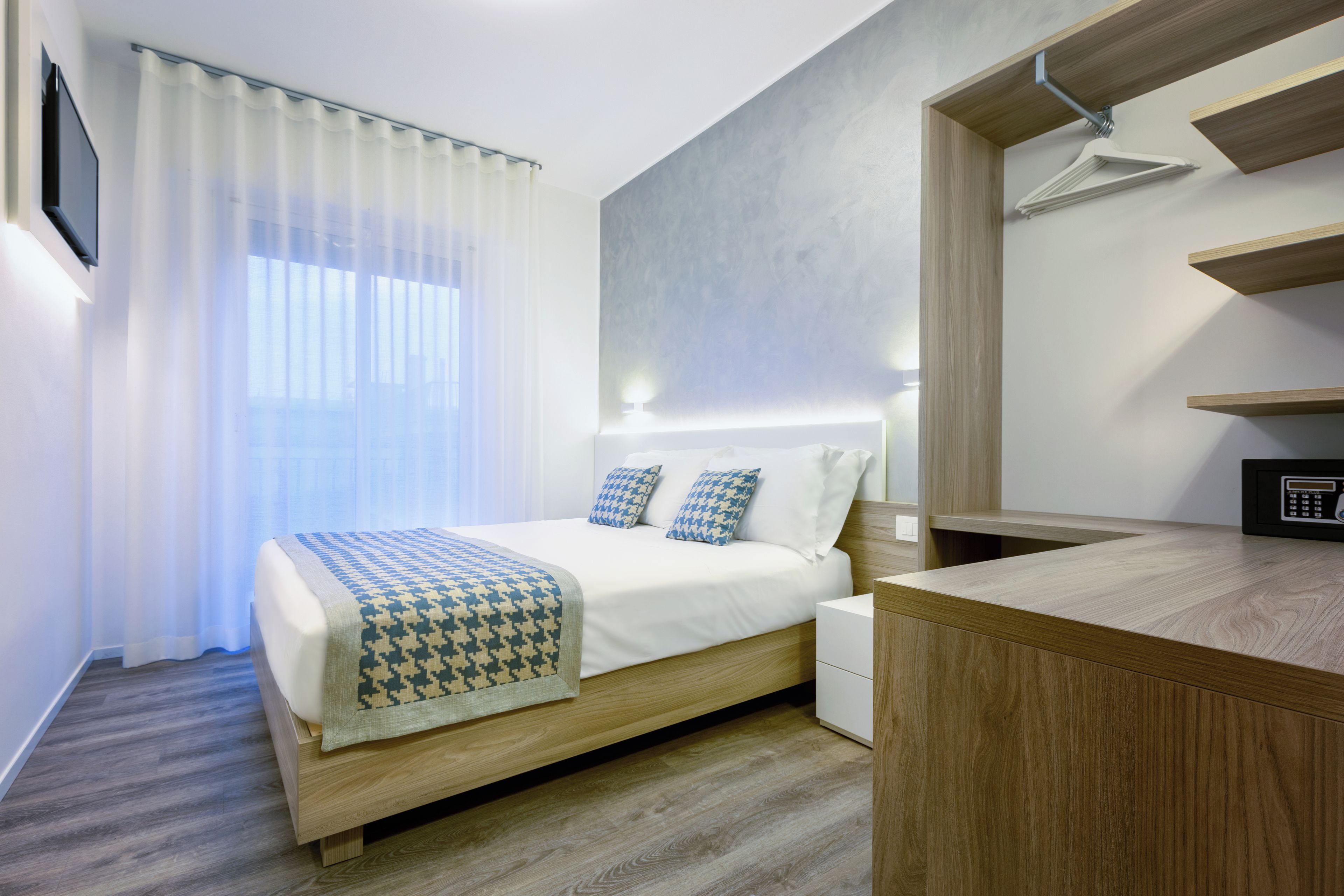 A modern hotel room with a bed, bedside table, and a built-in desk.