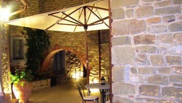 An outdoor patio area with stone walls, a table with chairs, and a large umbrella providing shade.