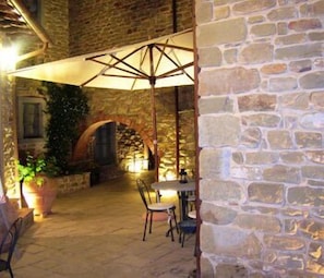 An outdoor patio area with stone walls, a table with chairs, and a large umbrella providing shade.
