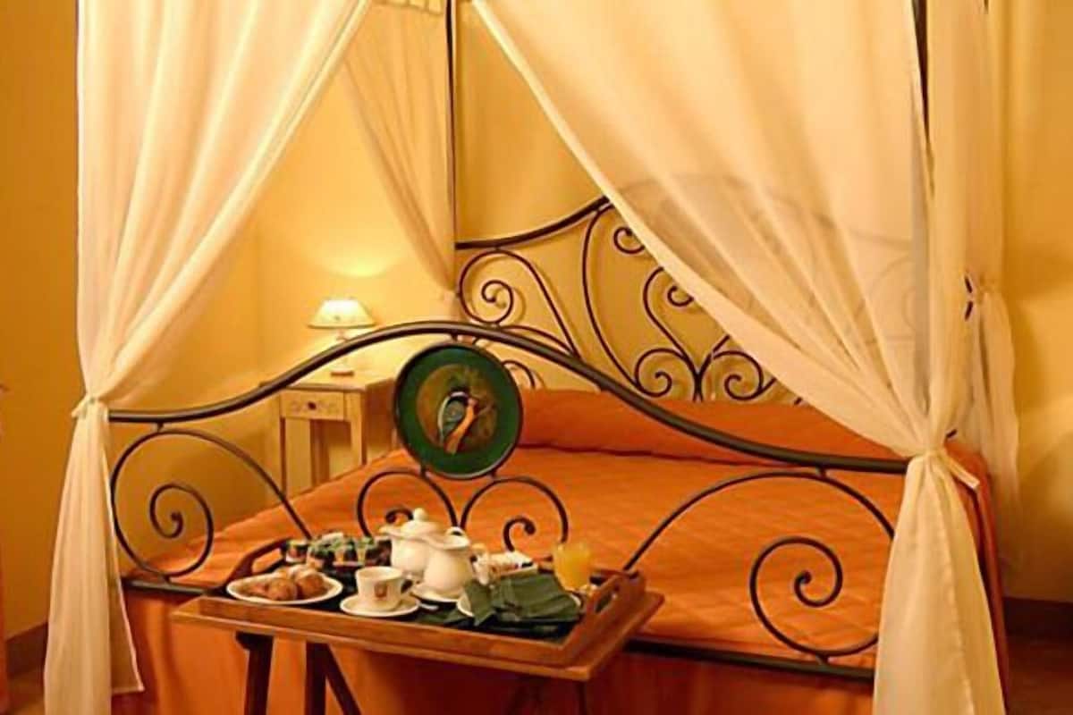 Un lit à baldaquin, une table de chevet avec une lampe et un plateau contenant des aliments pour le petit-déjeuner.