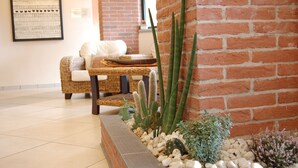 A room with a brick wall, a wicker sofa, a small cactus garden, and a framed picture on the wall. - Hotel Villa Glicini (San Secondo di Pinerolo)