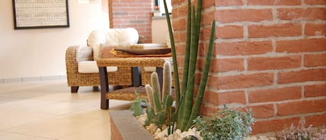 Una habitación con pared de ladrillo, sofá de mimbre, un pequeño jardín de cactus y un cuadro en la pared.