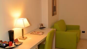 A small, modern room with a desk, a green chair, a television mounted on the wall, and a framed picture.