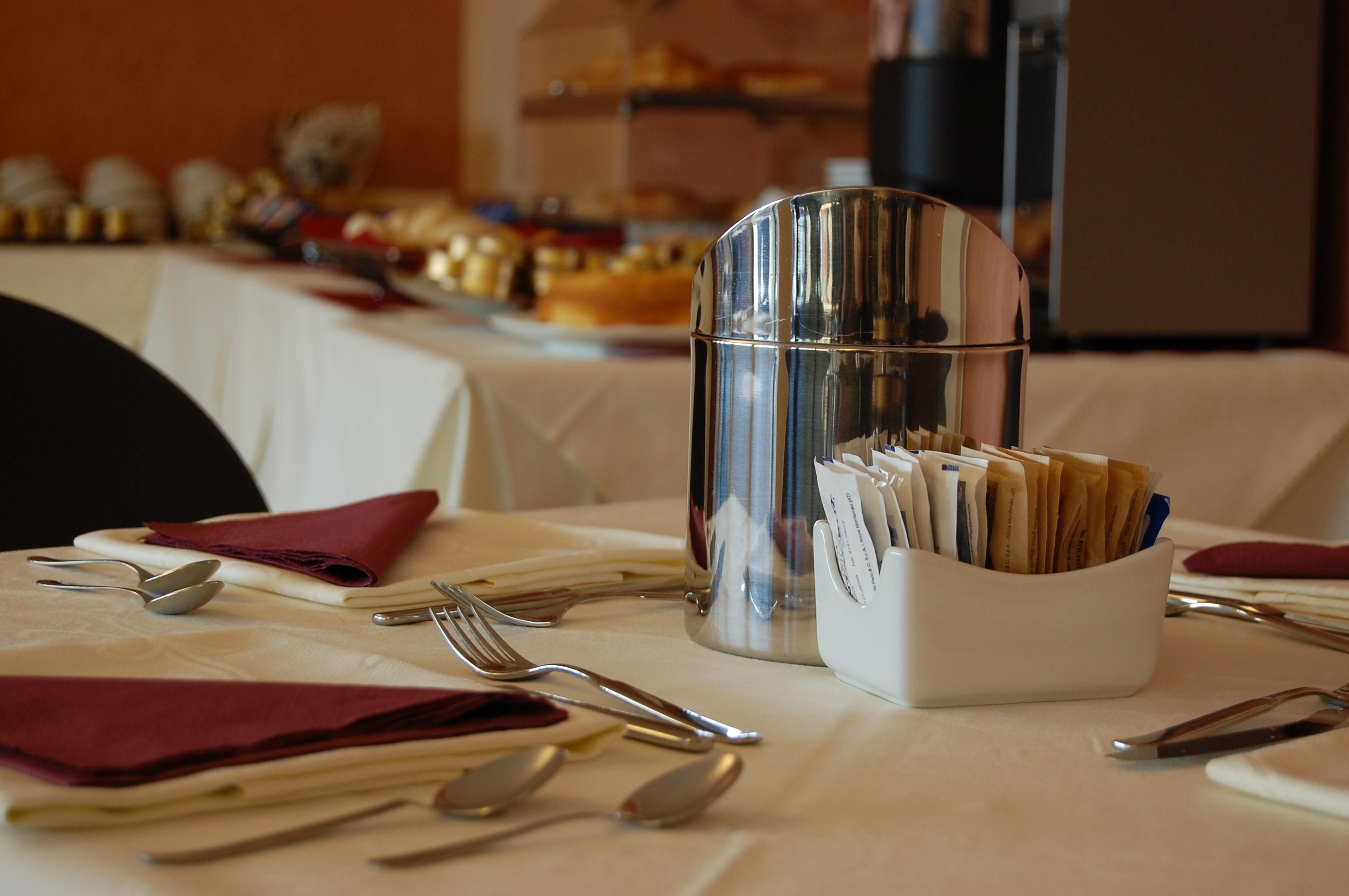 Une table dressée avec des couverts, un récipient en verre contenant des serviettes et un présentoir à menus.