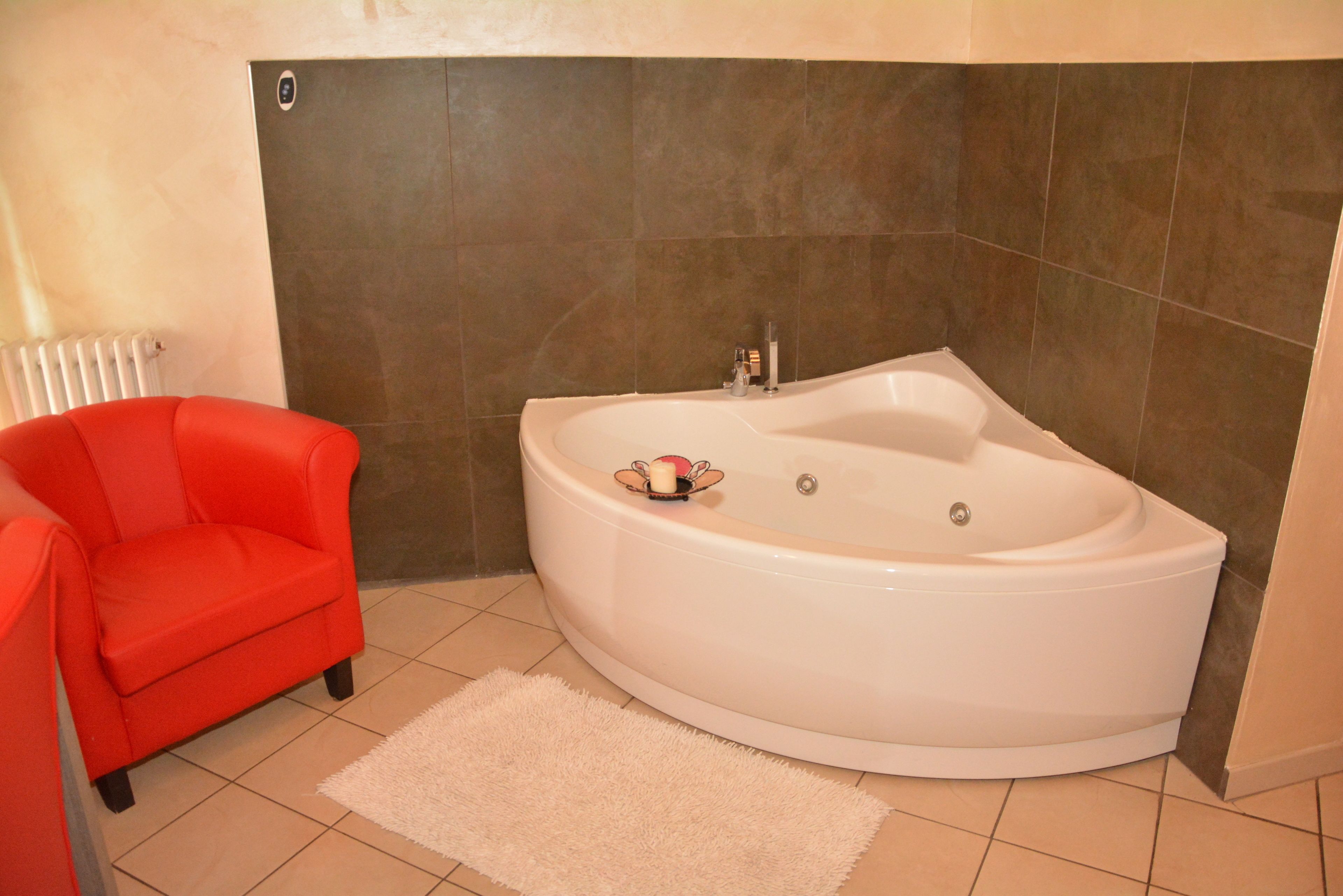 Un baño con una bañera grande, una silla roja y una alfombra blanca.