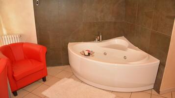 Un baño con una bañera grande, una silla roja y una alfombra blanca.