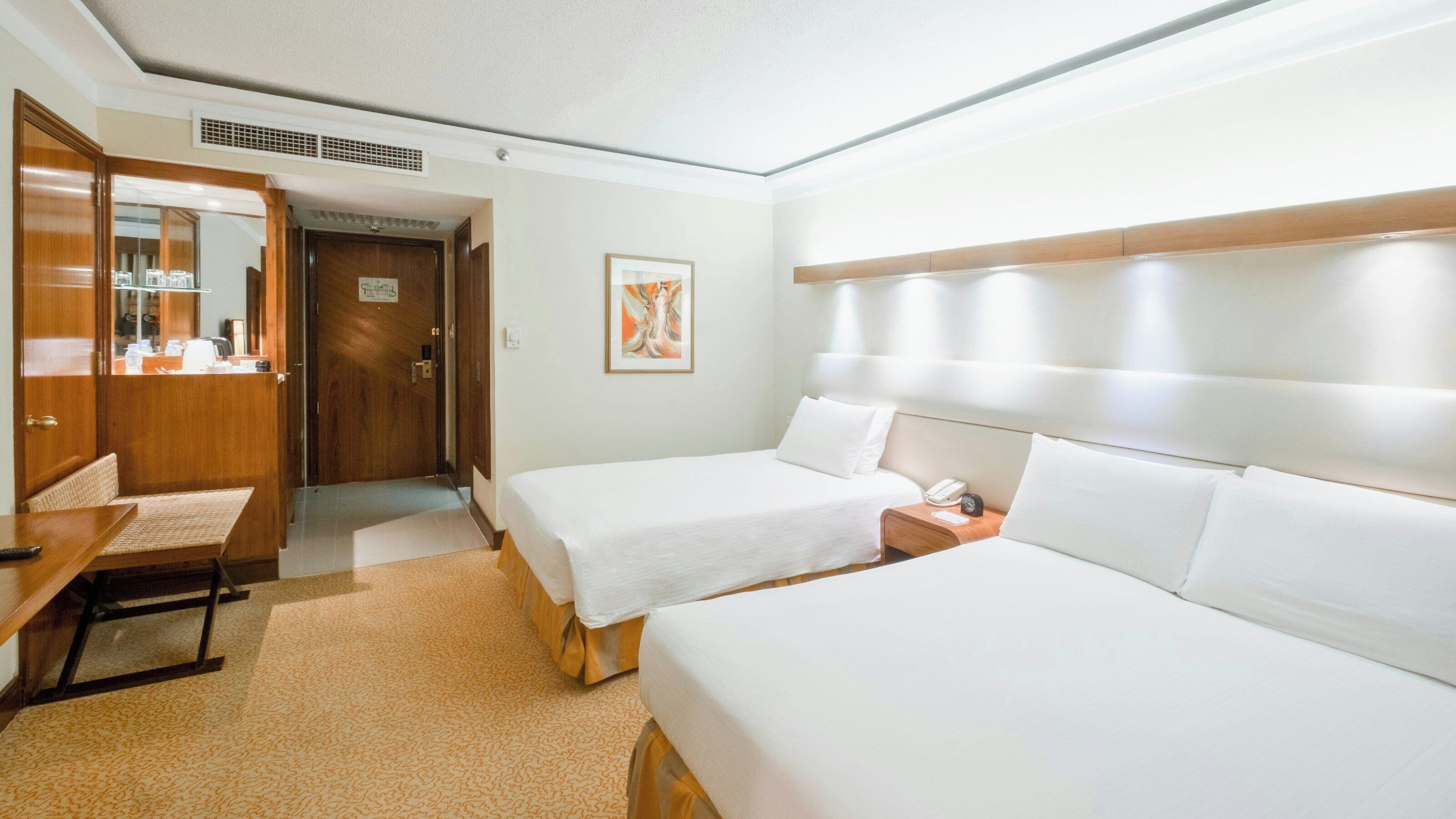 Habitación de hotel con dos camas, un escritorio, una silla, un espejo, un cuadro y una mesita de noche con un teléfono.