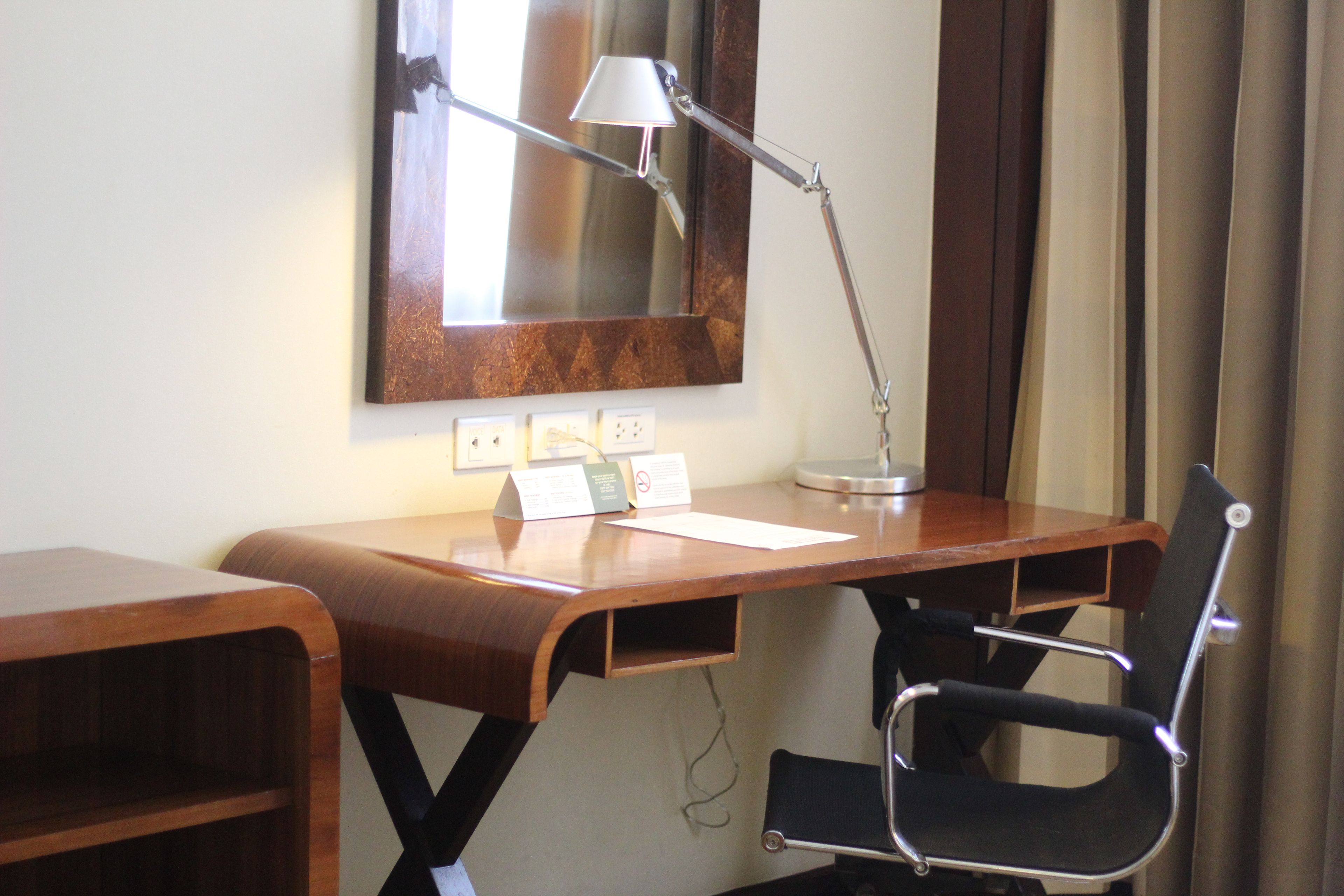 A wooden desk with a black office chair, a desk lamp, and a mirror above it.