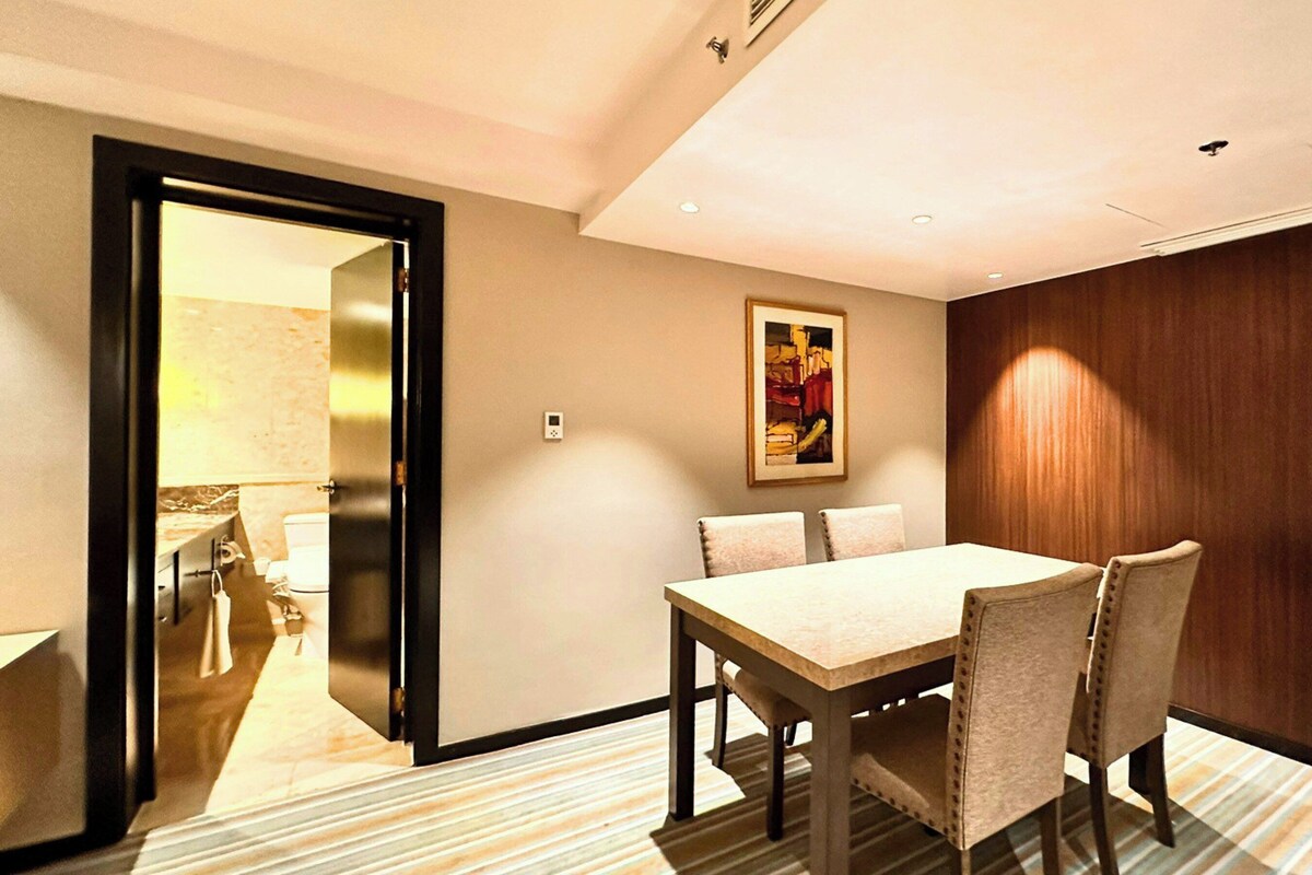Habitación de hotel con una mesa de comedor, sillas, un cuadro en la pared y paneles de madera.