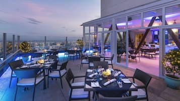 A rooftop restaurant with tables set for dining, overlooking a cityscape.