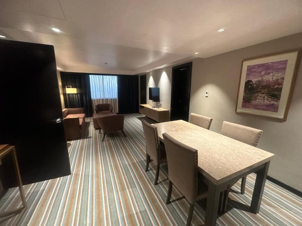 Une chambre d’hôtel avec un tapis à rayures, une table à manger avec des chaises, un téléviseur, un bureau et un tableau encadré au mur.