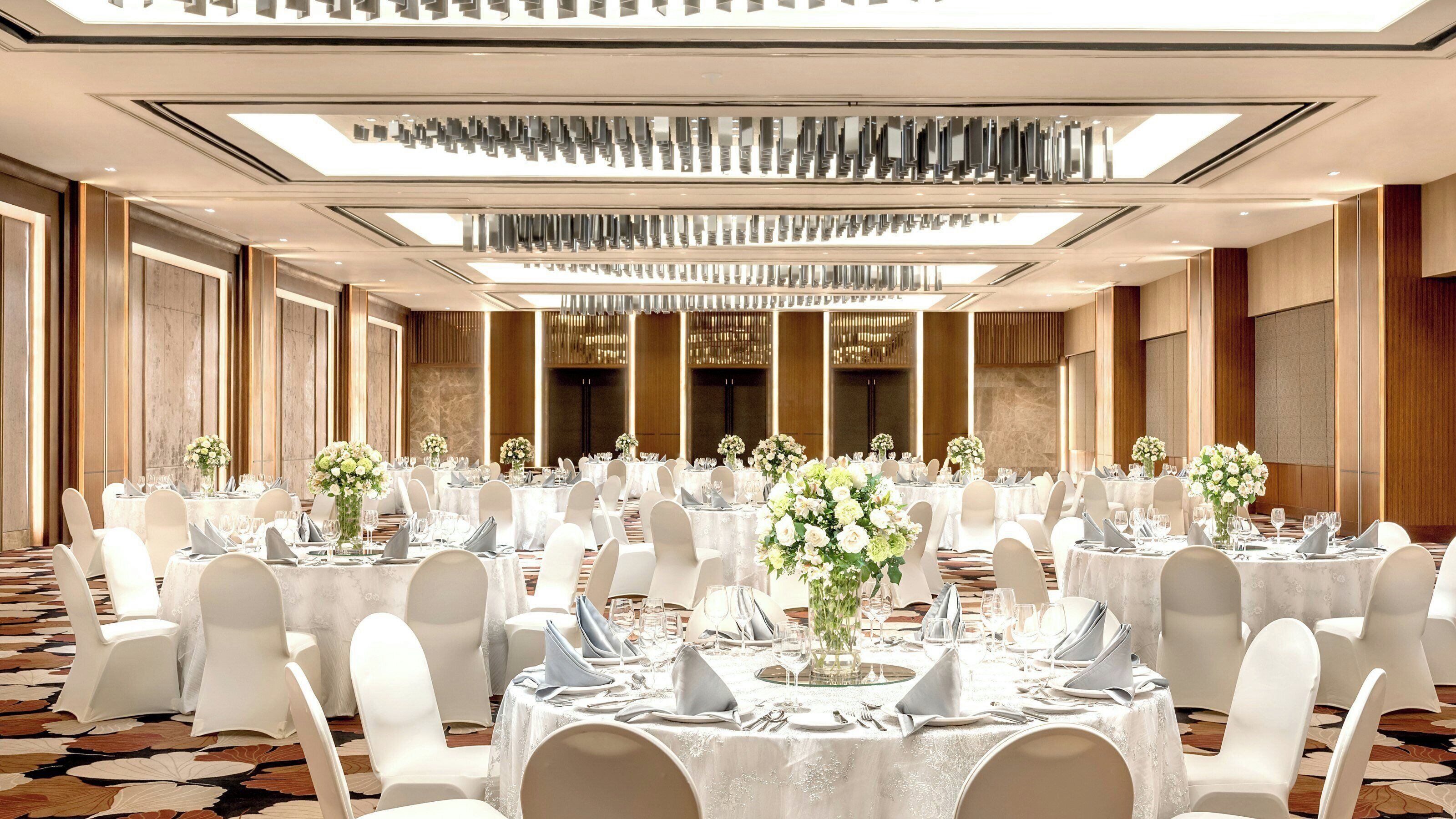 Un salón de banquetes con mesas redondas, sillas blancas y centros de mesa florales.