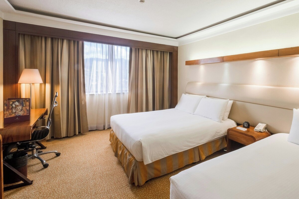 Een hotelkamer met twee bedden, een bureau met een lamp, een stoel en een telefoon op een nachtkastje.
