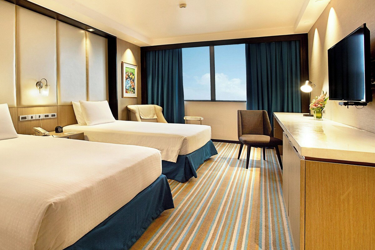 Een hotelkamer met twee bedden, een bureau, een stoel, een televisie en een raam met gordijnen.