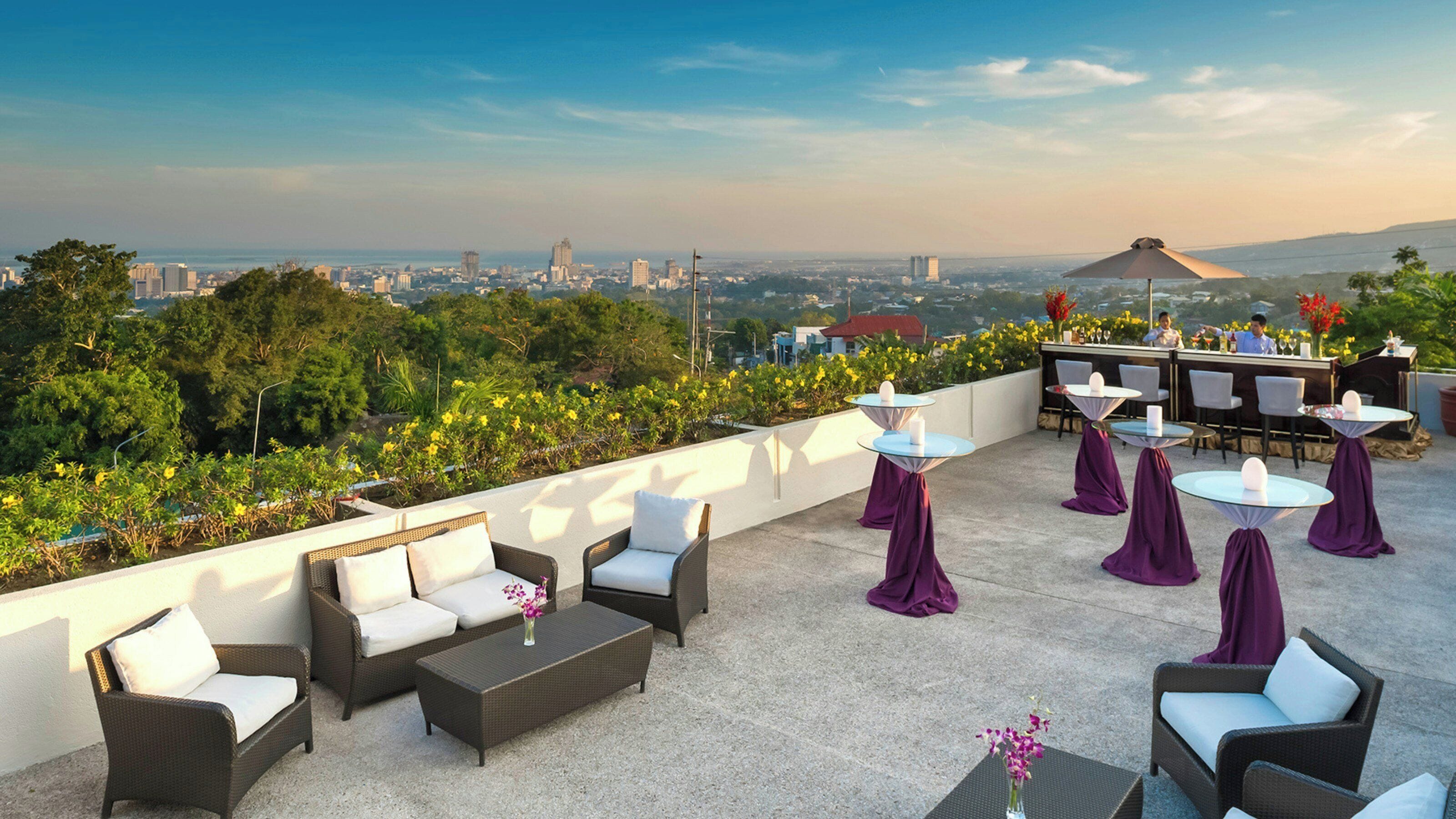 An outdoor terrace with seating, tables, and a view of a cityscape.