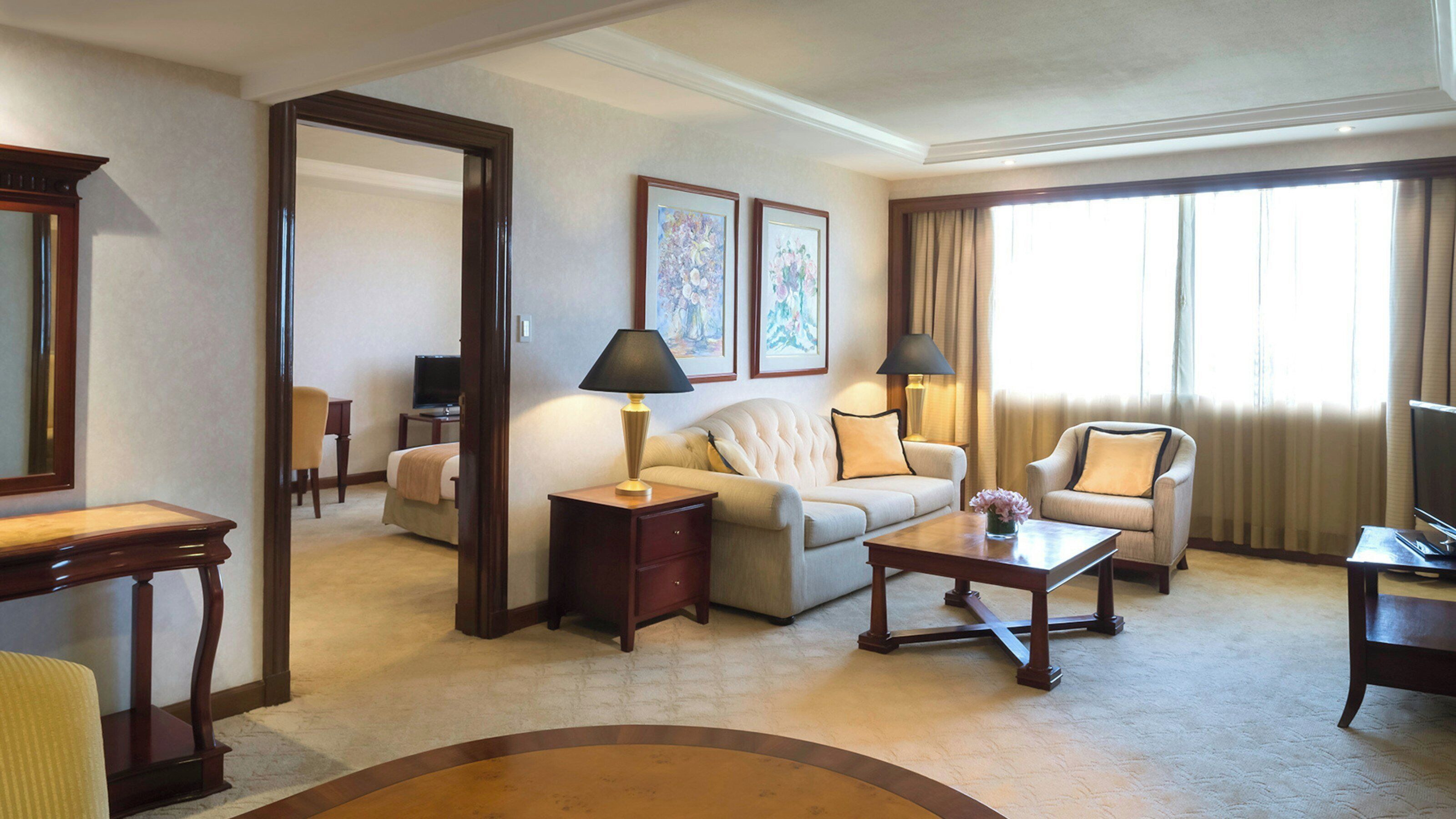 A hotel room with a sofa, armchairs, a coffee table, a TV, and artwork on the wall.