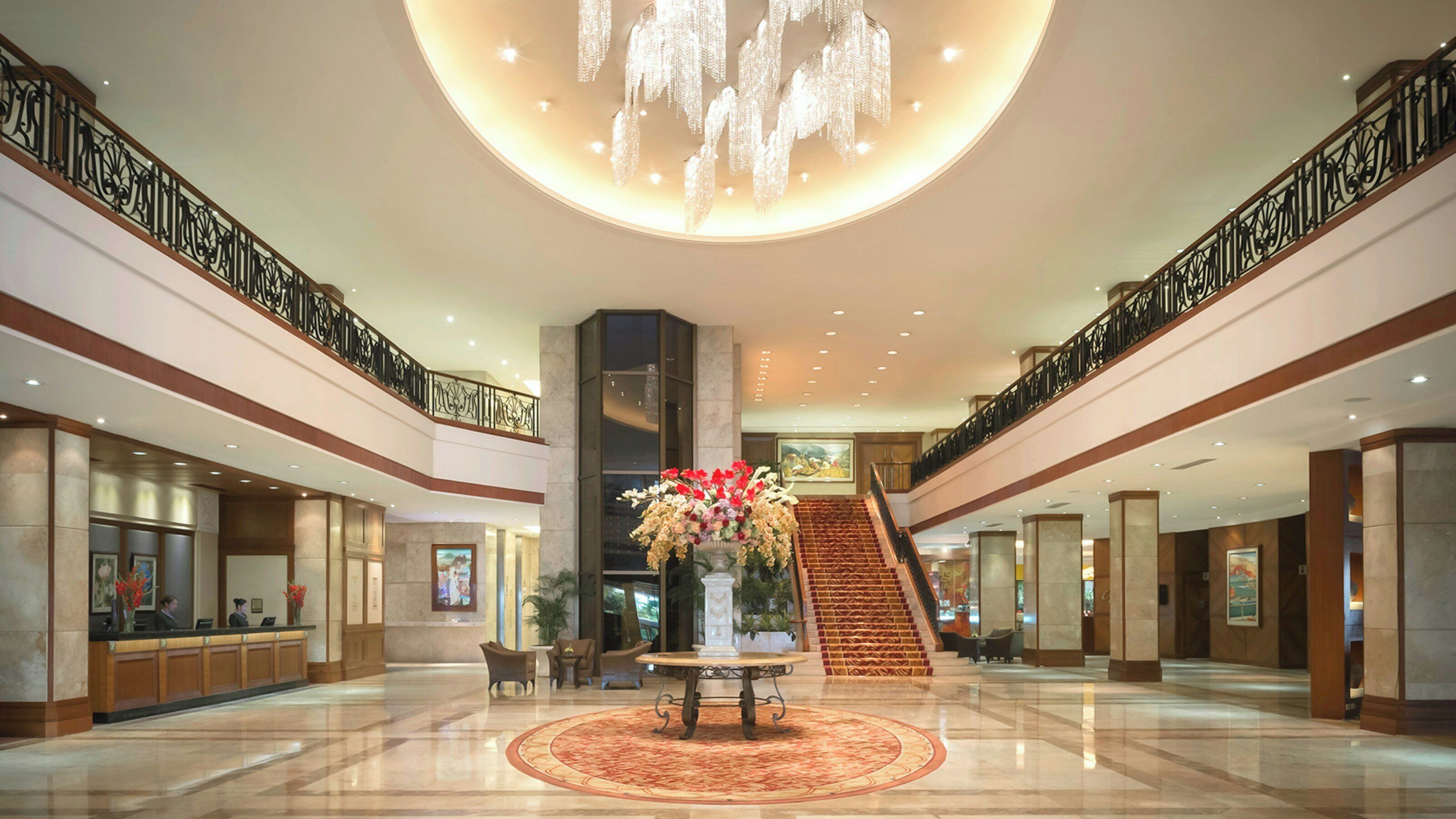 A spacious lobby with a central staircase, a reception desk, and a decorative chandelier.