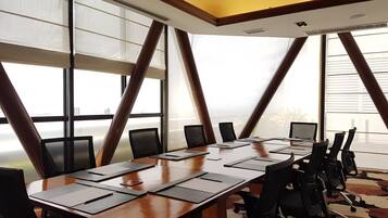 Un salón de conferencias con una larga mesa, varias sillas y amplios ventanales con persianas.