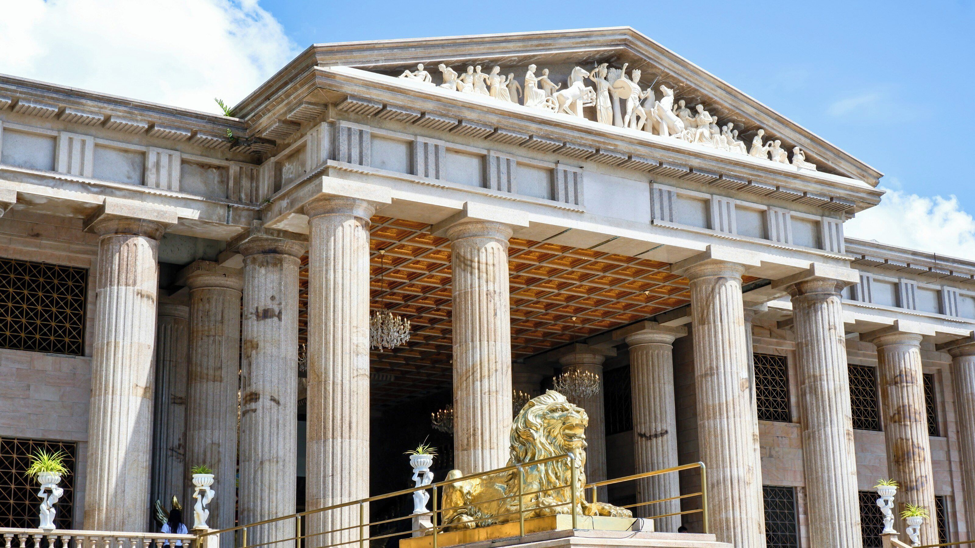 A classical building with columns, a central entrance, and a detailed sculpture above the doorway.