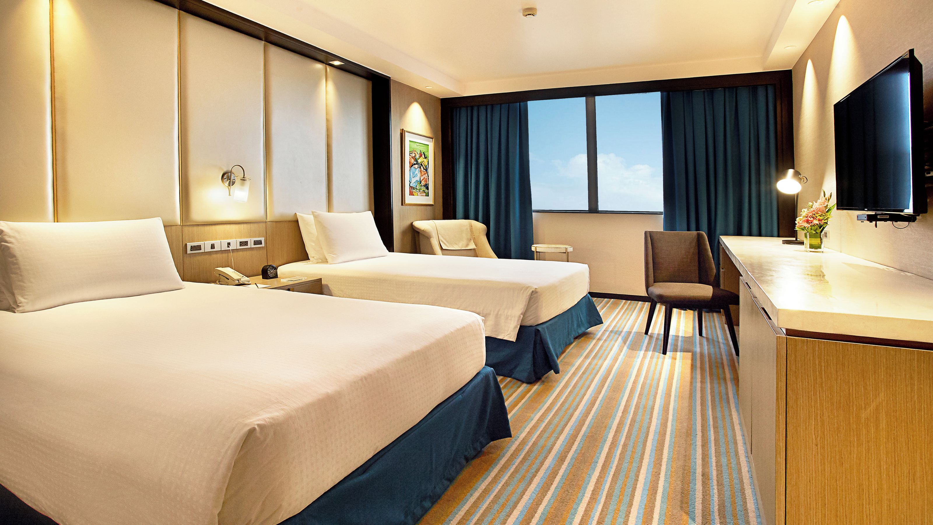 A hotel room with two beds, a desk, a chair, a television, and a window with curtains.
